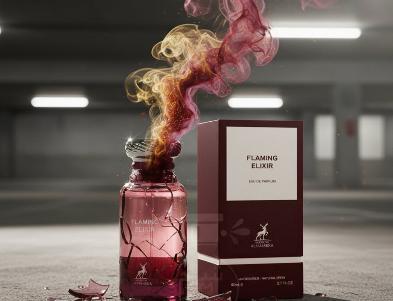 Maison Alhambra Flaming Elixir — Botol minyak wangi kaca retak dengan asap merah jambu dan emas meletup, sebelah kotak merah marunnya, di permukaan konkrit.