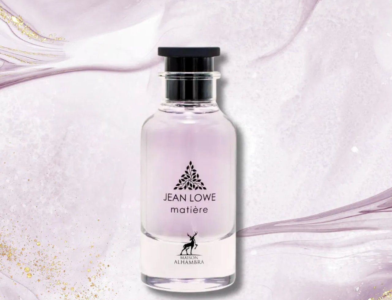 Maison Alhambra Jean Lowe Matiere — Botol minyak wangi kaca jernih berisi cecair ungu lembut, penutup hitam, dan label berlogo pokok serta siluet rusa. Latar belakang mempunyai corak marmar ungu dan putih abstrak dengan kilauan emas.