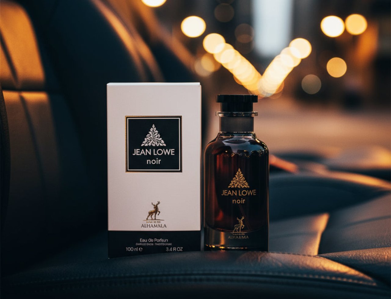 Maison Alhambra Jean Lowe Noir — A dark glass perfume bottle and its white box packaging are placed on a dark leather surface, with blurred city lights in the background.