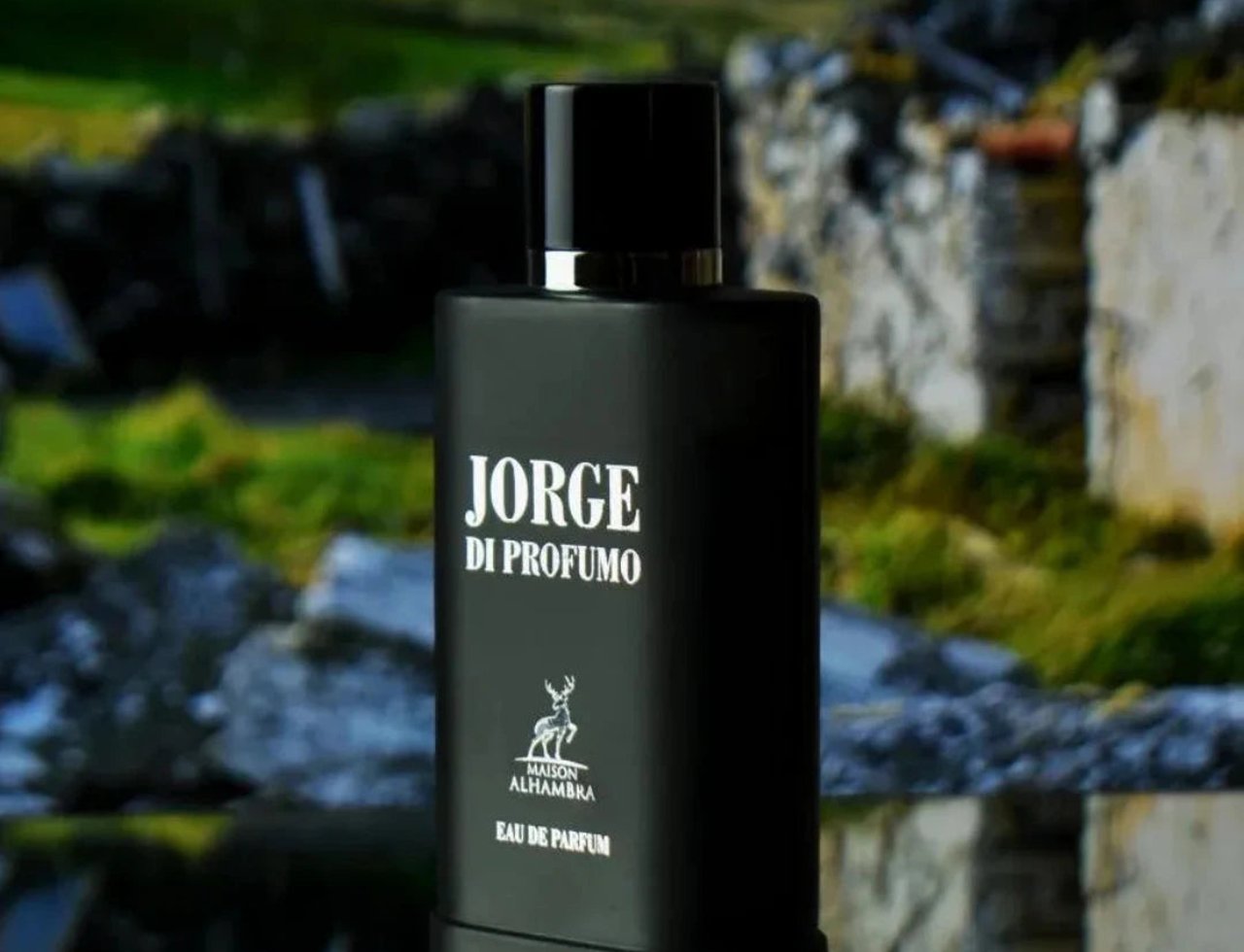 Maison Alhambra Jorge Di Profumo — Black matte perfume bottle with silver accents, featuring 'Jorge Di Profumo' and a deer logo, set against a blurred background of stone ruins and greenery.