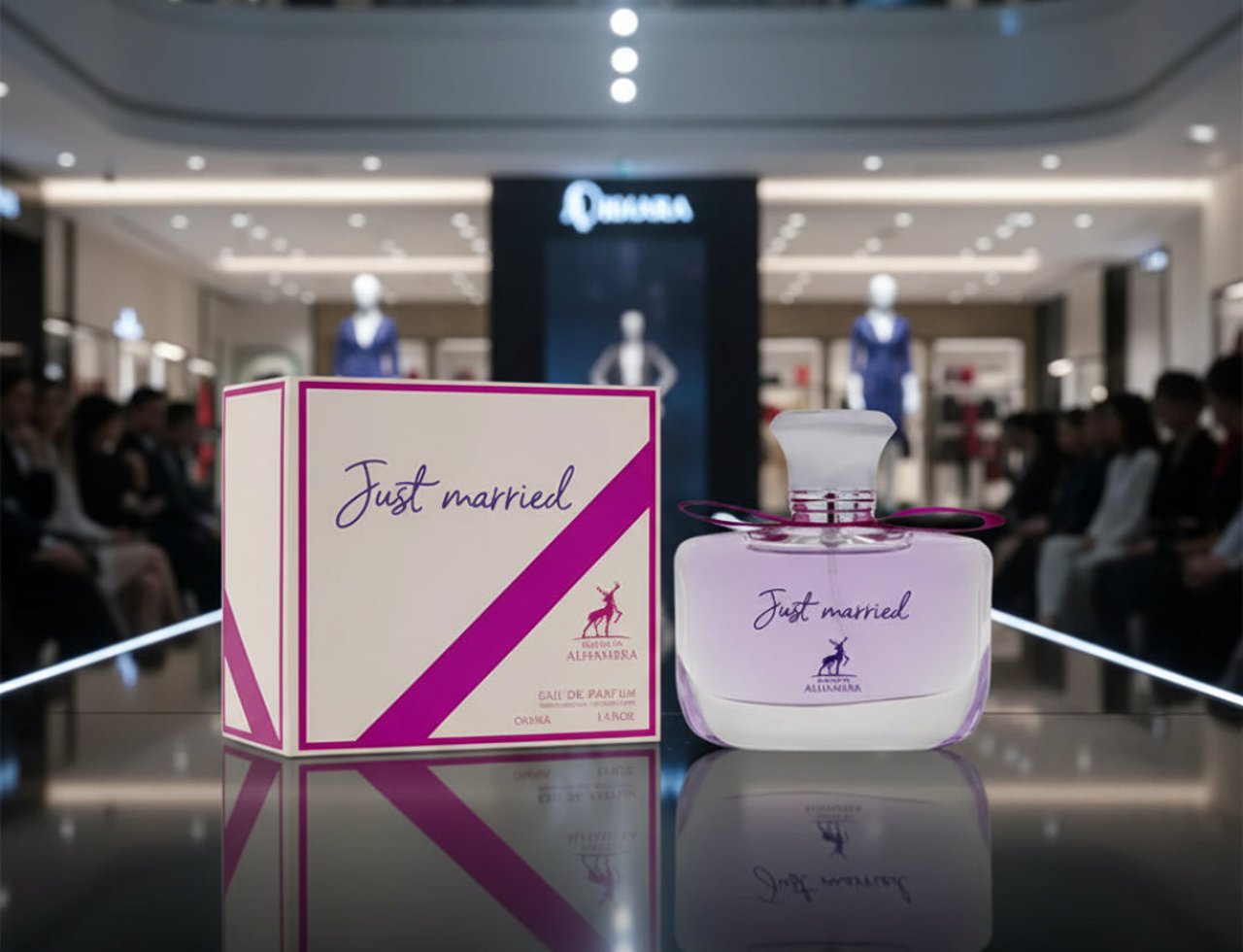 Maison Alhambra Just Married by Maison Alhambra Woman 100ml — A perfume bottle and its box displayed on a reflective surface, with a blurred mall background.