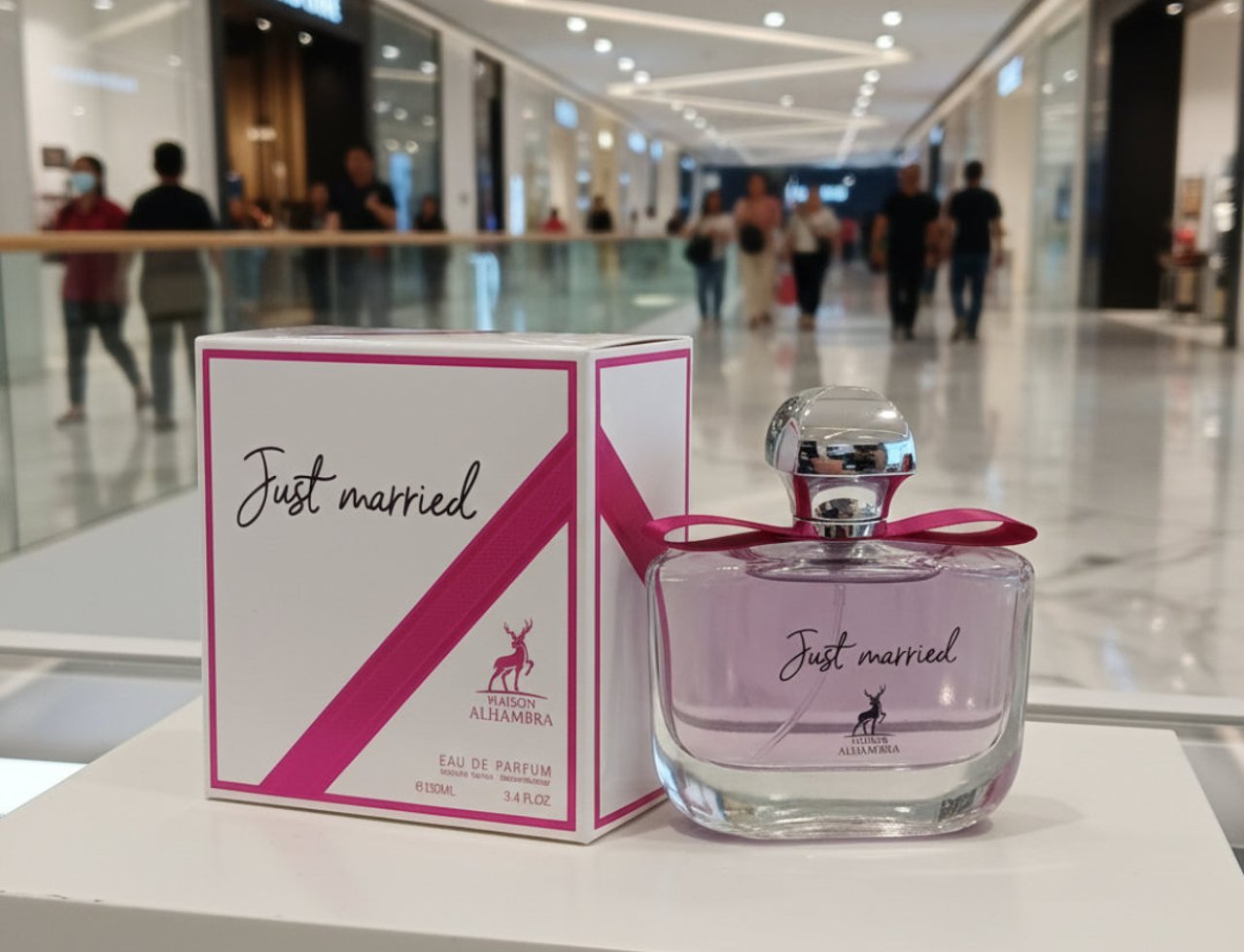 Maison Alhambra Just Married by Maison Alhambra Woman 100ml — Kotak putih dengan reben merah jambu dan botol minyak wangi kaca jernih berisi cecair merah jambu serta penutup perak, dipamerkan di dalam pusat beli-belah.