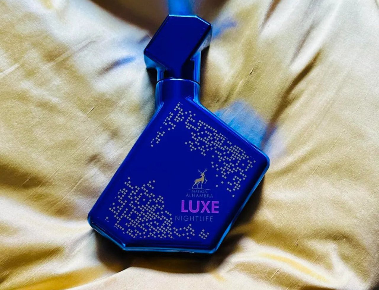 Maison Alhambra Luxe Nightlife by Maison Alhambra Unisex 100 ml — Blue glass perfume bottle with gold dot pattern and deer logo, resting on a golden satin fabric.