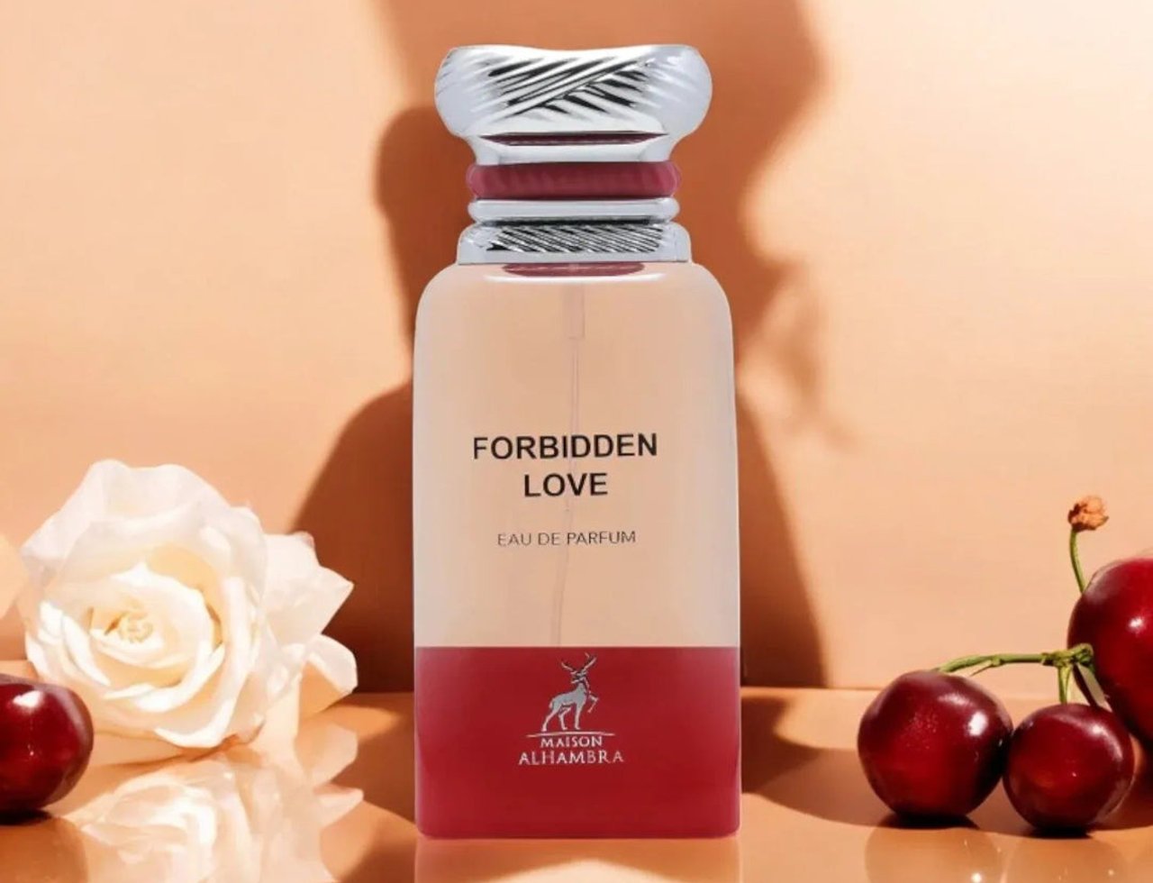 Maison Alhambra Forbidden Love by Maison Alhambra 80ml EDP Women — Botol minyak wangi kaca jernih dengan penutup berjalur perak dan aksen merah, tertulis 'FORBIDDEN LOVE EAU DE PARFUM' dan logo rusa. Diletakkan di atas permukaan memantul dengan bunga ros putih dan buah ceri.