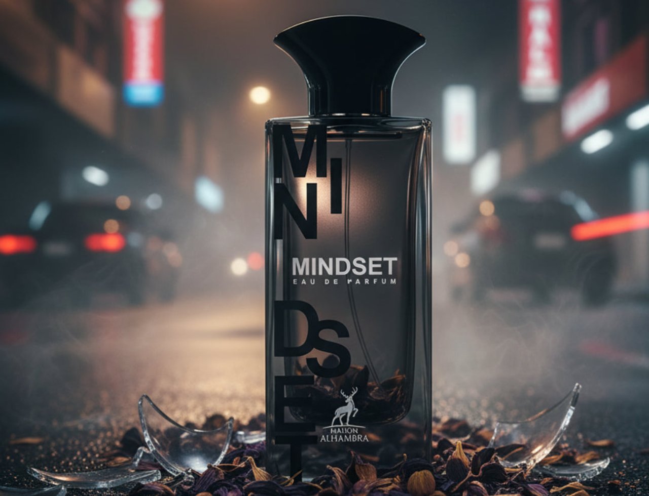 Maison Alhambra Mindset by Maison Alhambra – 100 ml For Man, botol minyak wangi kaca gelap berlabel "MINDSET", dikelilingi serpihan kaca pecah dan bunga kering di permukaan gelap basah dengan lampu bandar dan kereta kabur di latar belakang.
