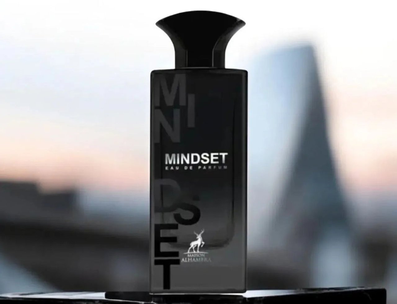 Maison Alhambra Mindset by Maison Alhambra – 100 ml For Man, a black rectangular bottle with 'MINDSET EAU DE PARFUM' text and a deer logo, set on a dark marble surface with a blurred cityscape background.