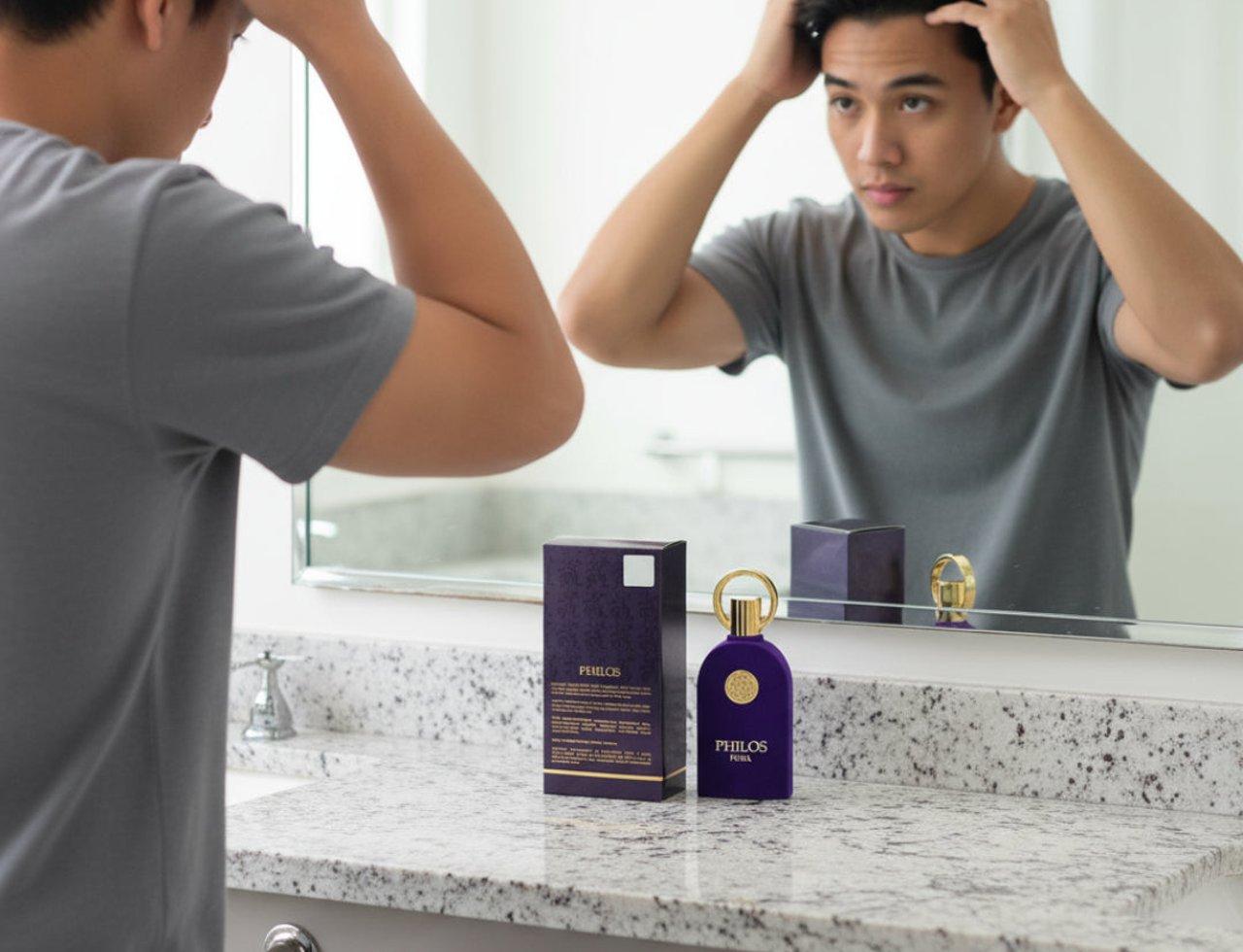 Maison Alhambra Philos Pura by Maison Alhambra 100ml EDP Man — A young man styles his hair in front of a mirror, with a purple perfume bottle and its box displayed on a granite countertop.