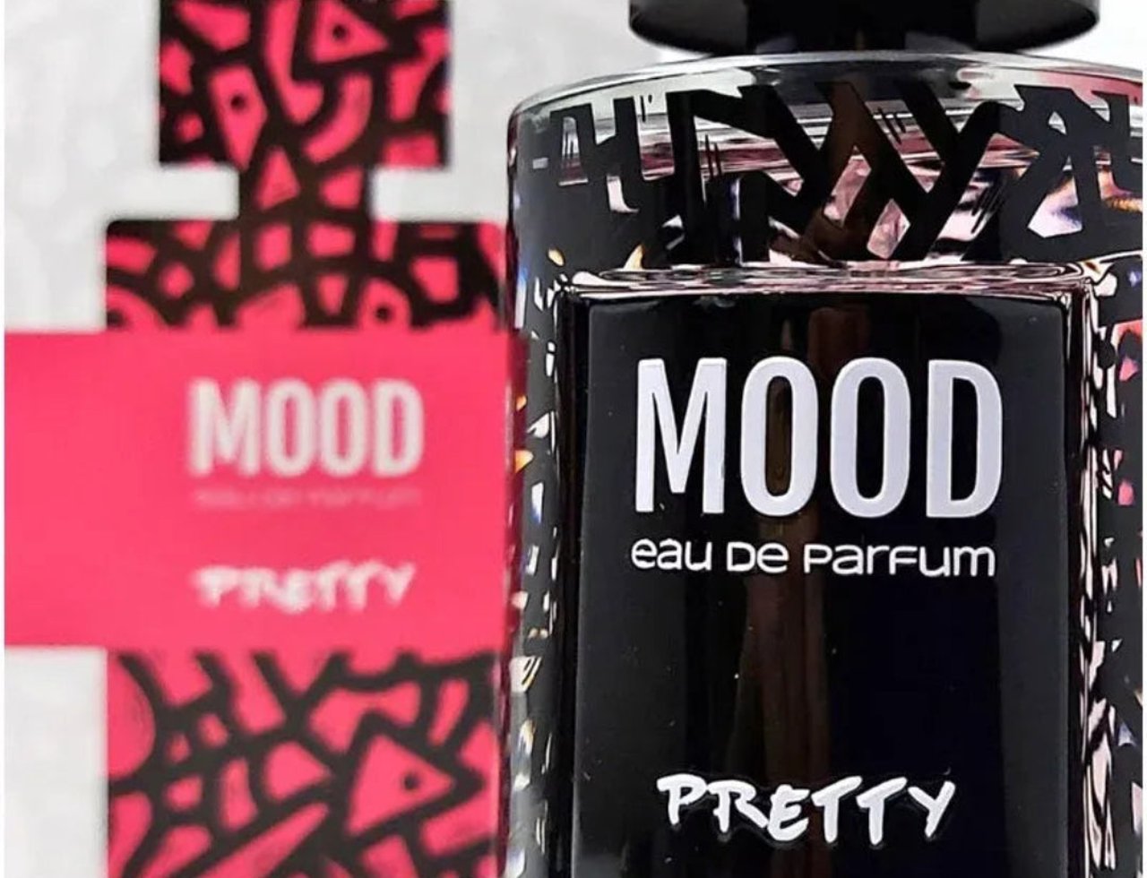 Mood Perfume Mood Pretty For Her 100 ml EDP — Close-up of a black perfume bottle with a black and pink abstract pattern, and the text "MOOD eau de Parfum PRETTY" on the label. A blurred pink box with the same pattern and "MOOD PRETTY" text is visible in the background.