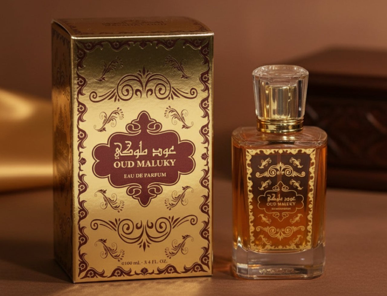 Nafahat Oud Maluky by Nafahat 100ml Unisex — Kotak emas berhias dan botol minyak wangi kaca bertutup emas, cecair perang, di atas permukaan bertekstur coklat dan fabrik sutera.