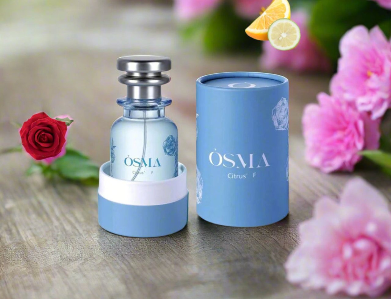 Osma Osma Citrus F 75ml Eau de Parfum — Botol minyak wangi biru muda bertudung perak dan kotak silinder biru, dikelilingi bunga ros merah jambu serta hirisan oren dan limau.