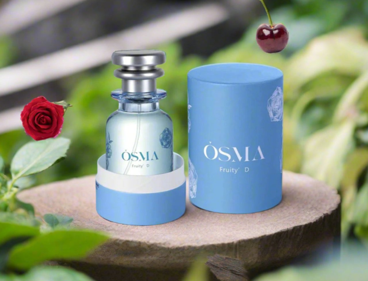 Osma Fruity D Cherry & Oud 75ml EDP — Perfume bottle and its cylindrical box on a wooden stand, with a red rose and a cherry floating in the background.