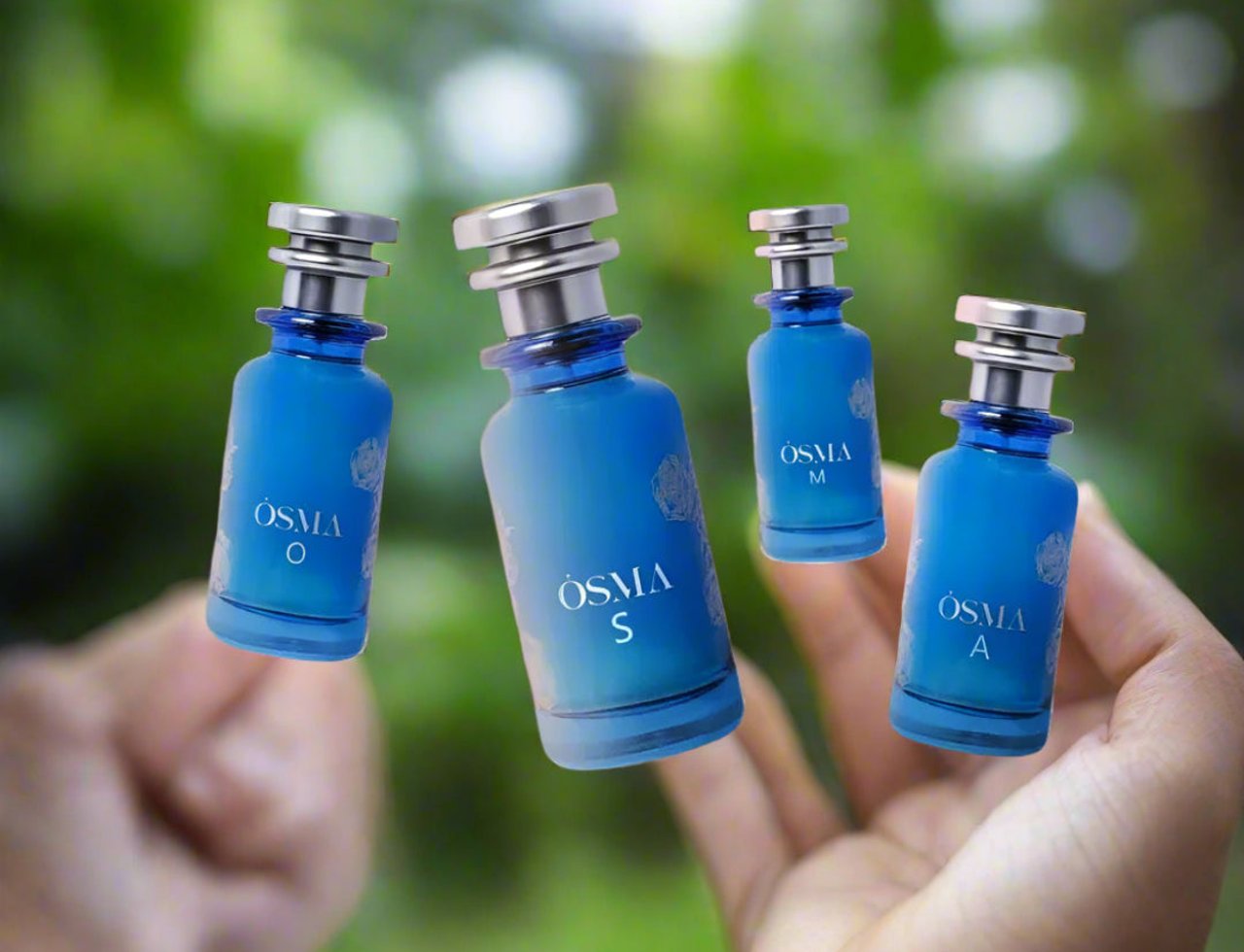 Osma Osma O Tobacco & Pear 150ml EDP — Empat botol kecil minyak wangi biru bertutup perak terapung di atas tangan seseorang berlatar belakang hijau kabur.
