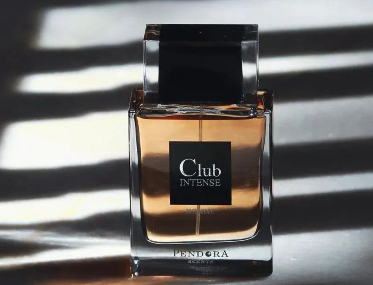 Pendora Club Intense 100ml EDP Men Paris Corner — Botol minyak wangi kaca segi empat dengan cecair perang, penutup hitam, dan label hitam bertulis 'Club Intense' dan 'HOMME', berlatar belakang belang cahaya dan bayang mendatar yang kuat.
