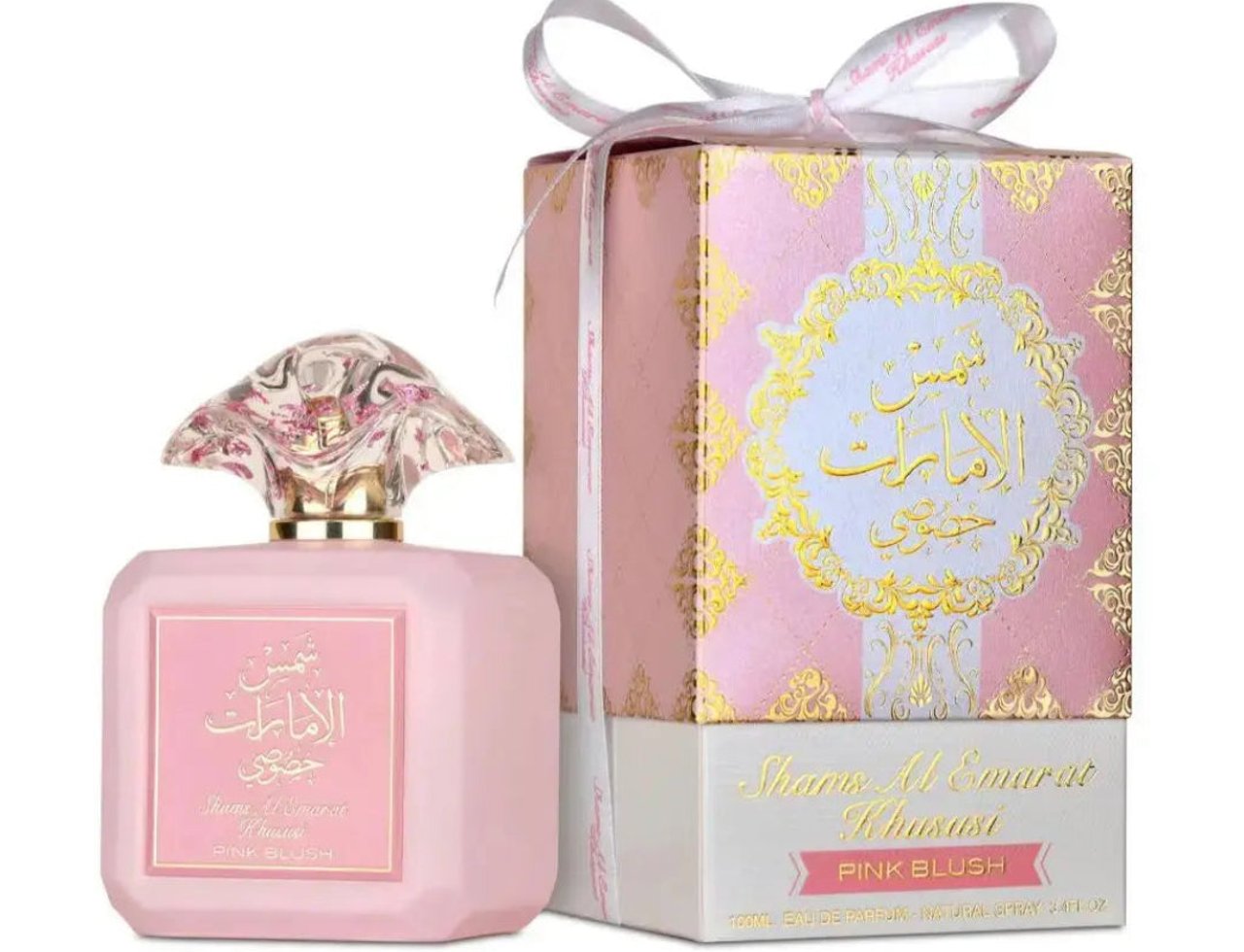 Ard Al Zaafaran Shams Al Emarat Khususi Pink Blush 100ml — Botol minyak wangi merah jambu dengan penutup jernih berfaset, bersebelahan kotak hadiah corak merah jambu dan emasnya yang diikat dengan reben putih.