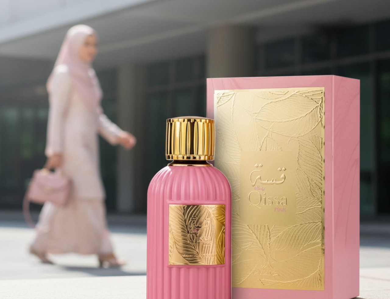Paris Corner Qissa Pink by Paris Corner 100ml for Women — Pink fluted perfume bottle with gold cap and gold embossed label, next to its pink and gold box, with a blurred woman in a hijab walking in the background.