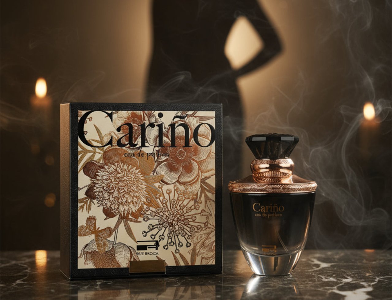 Rue Broca Carino Black Pour Femme EDP — Botol minyak wangi hitam dengan penutup emas dan kotak corak bunga yang rumit, diletakkan di atas permukaan marmar dengan kesan asap dan bayangan siluet wanita di latar belakang.