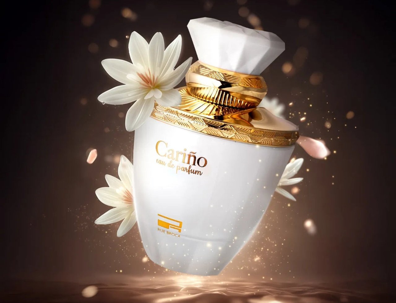 Rue Broca Carino White Pour Femme 100ml EDP — Botol minyak wangi putih dengan perincian emas, dihiasi bunga putih dan cahaya emas berkilauan berlatar belakang gelap.
