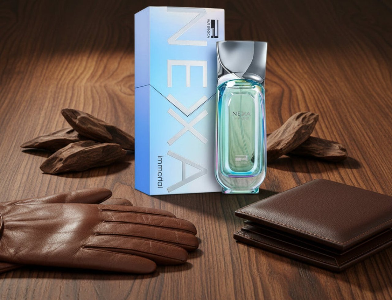 Nexa Immortal by Rue Broca — A clear glass perfume bottle with a gradient blue and white box, brown leather gloves, brown leather wallet, and oud wood pieces on a wooden surface.