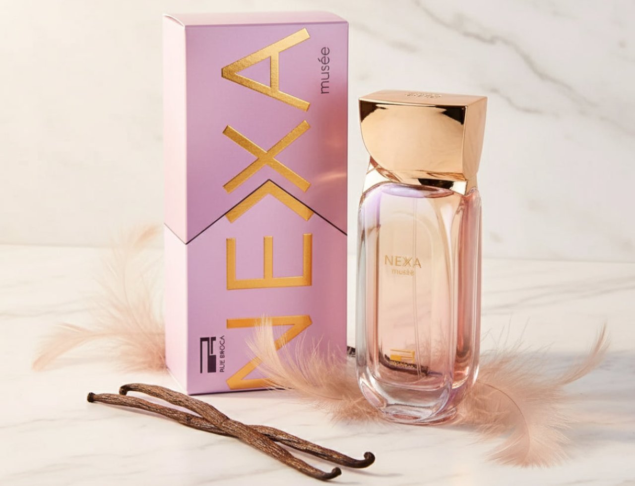 Rue Broca Nexa Musee by Rue Broca – 100 ml for Women — Kotak dan botol minyak wangi berwarna merah jambu dan emas dengan penutup emas, di atas latar belakang marmar bersama dua batang vanila dan bulu halus berwarna merah jambu.