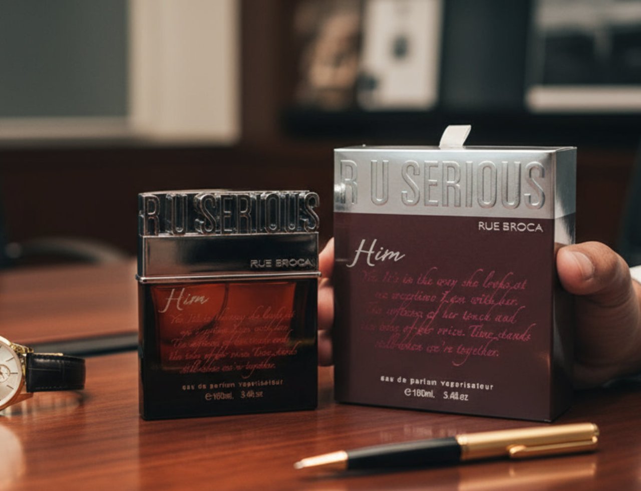 Rue Broca R U Serious Him Rue Broca 100ml EDP Men — A dark glass perfume bottle and its maroon box sit on a wooden desk next to a gold and black pen and a watch.
