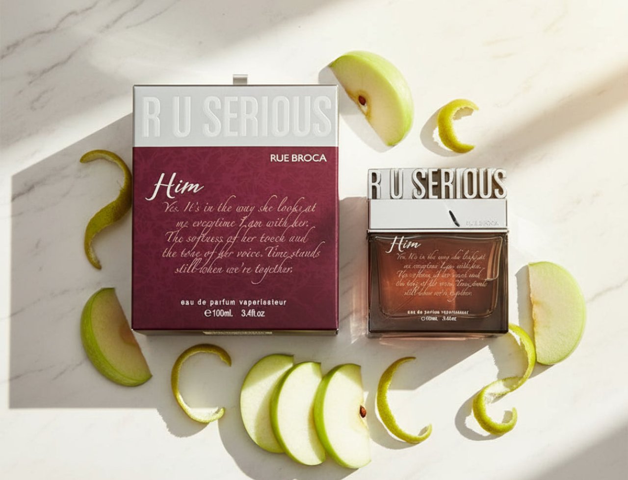 Rue Broca R U Serious Him EDP Lelaki — Kotak dan botol pewangi bersama hirisan epal dan kulit lemon berlingkar di atas latar marmar