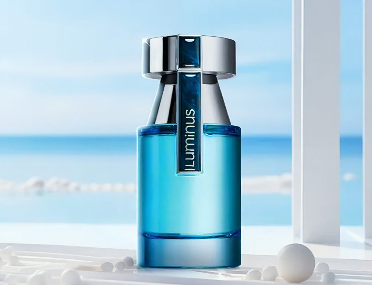 Rue Broca Luminus Pour Homme by Rue Broca 100ml Lelaki — Botol minyak wangi kaca biru dengan penutup perak, berlatar belakang laut dan langit kabur, dengan sfera hiasan putih di latar depan.