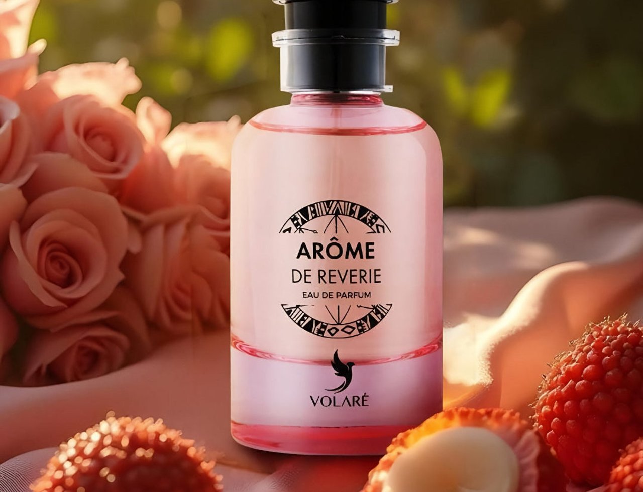 Volare Arome de Reverie Eau de Parfum — Botol minyak wangi merah jambu bertudung hitam, dikelilingi bunga ros merah jambu dan laici di atas kain satin.