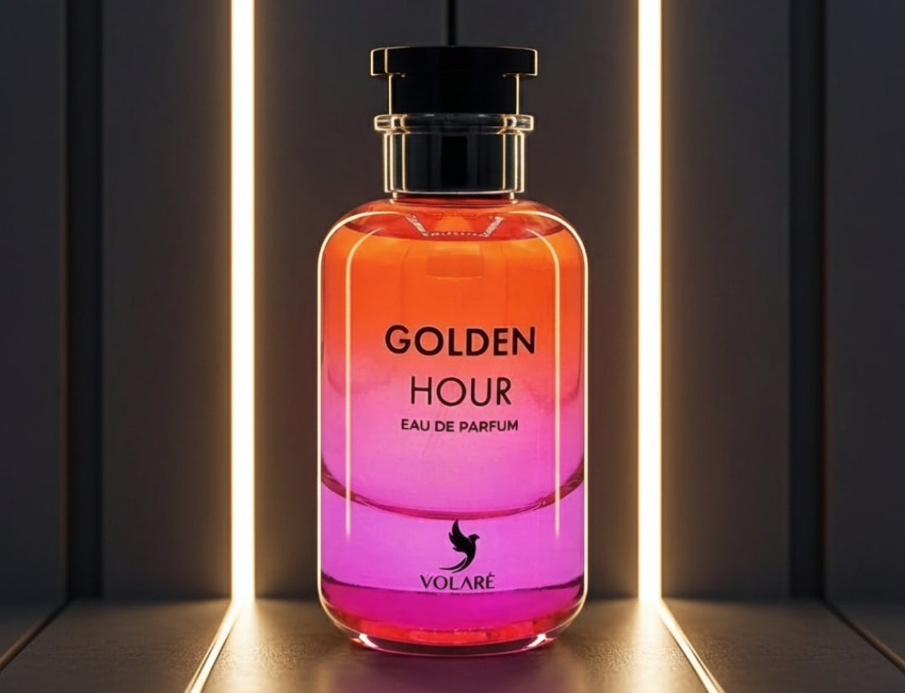 Volare Golden Hour by Volare 100ml EDP for Her — Botol minyak wangi gradien dengan cecair oren dan merah jambu, penutup hitam, dan logo burung, berlatar belakang gelap dengan lampu putih menegak.