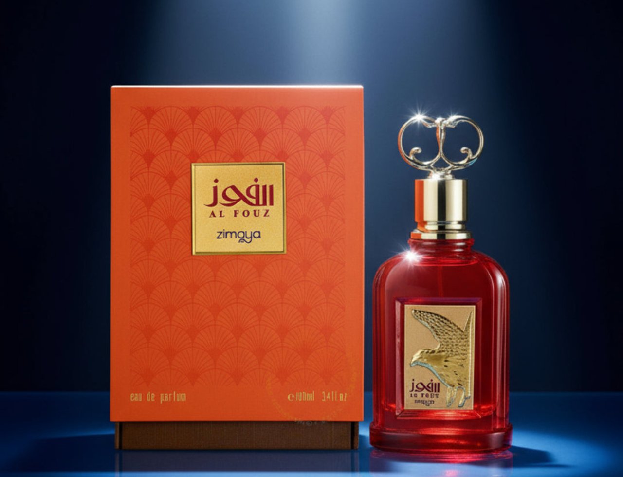 Zimaya Al Fouz by Zimaya 100ml EDP Unisex — Kotak corak oren dan botol minyak wangi kaca merah dengan lambang helang emas dan penutup emas berhias, di latar belakang biru gelap.