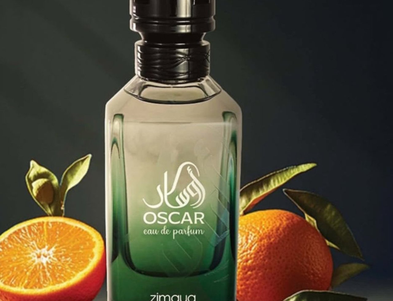 Zimaya Oscar by Zimaya 100ml EDP Men — A clear glass perfume bottle with a black cap, featuring green gradient liquid, with a sliced orange and whole orange, cardamom pods, and peppercorns arranged around it.
