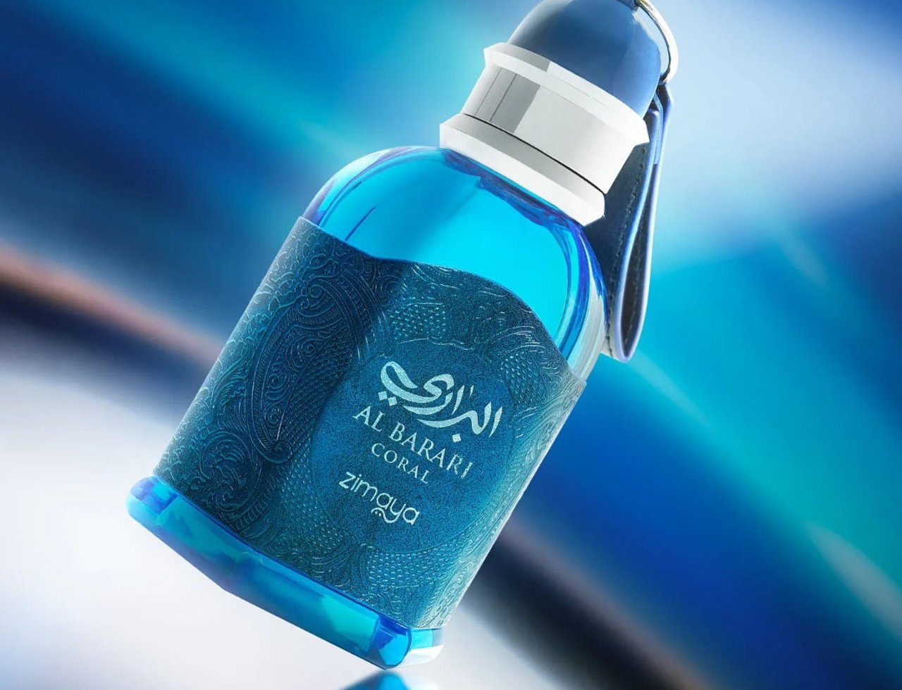 Zimaya Al Barari Coral by Zimaya 100 ml EDP — A blue glass perfume bottle with an ornate blue label, featuring Arabic script and "AL BARARI CORAL" text, tilted against a blurred blue background.