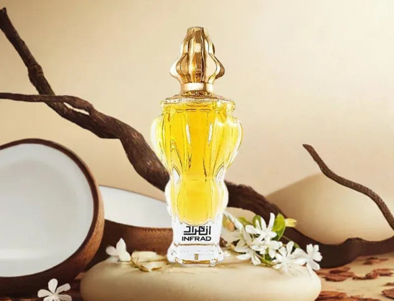 Zimaya Infrad Luxe by Zimaya 100ml EDP for Women — A golden-capped perfume bottle with yellow liquid, placed on a stone pedestal, surrounded by dried branches, coconut shell halves, and white flowers.