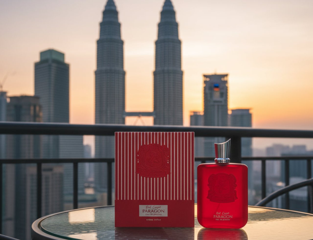 Zimaya Red Carpet Paragon EDP 100ml — Botol dan kotak minyak wangi merah dipamerkan di atas meja kaca dengan latar belakang Menara Berkembar Petronas ketika matahari terbenam.