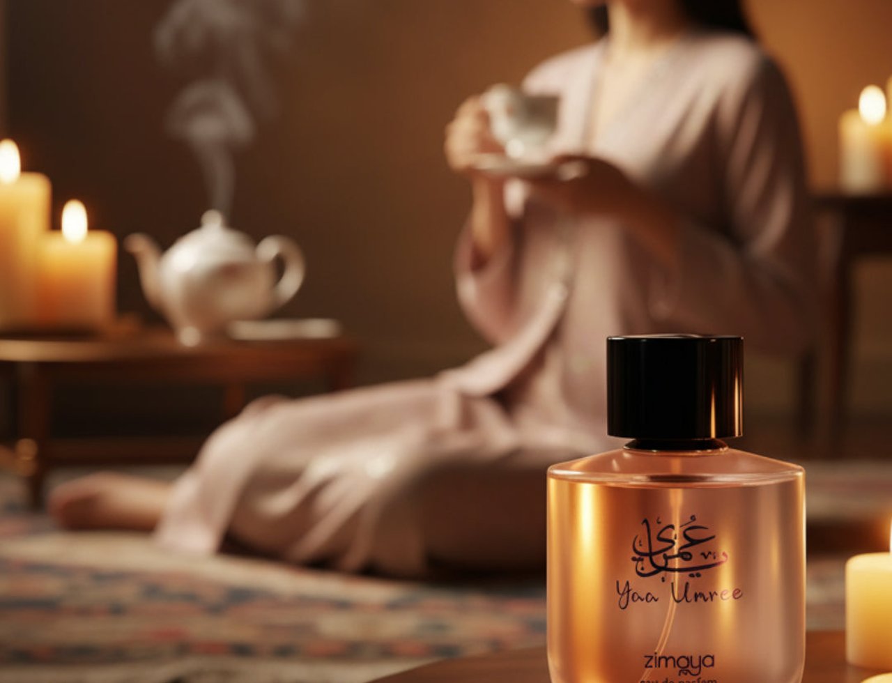 Yaa Umree by Zimaya EDP 100 ml Women — A clear glass perfume bottle with a black cap sits on a wooden table, with a woman in a pink robe holding a teacup in the blurred background, surrounded by lit candles and a teapot.