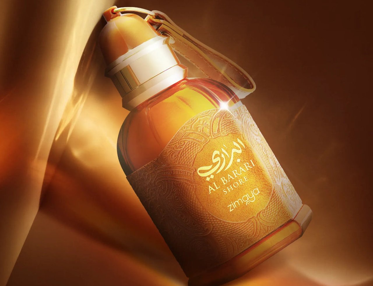 Zimaya Al Barari Shore — Botol minyak wangi kaca amber dengan penutup emas dan label bertekstur, bersandar pada fabrik emas berlipat.