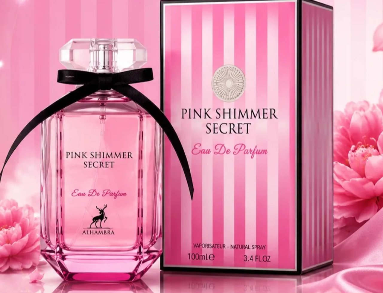 Maison Alhambra Pink Shimmer Secret 100ml — A pink perfume bottle with a black ribbon and a faceted clear cap, next to its pink and white striped box, with pink flowers and satin fabric in the background. | Maison Alhambra Pink Shimmer Secret 100ml — Botol minyak wangi merah jambu dengan reben hitam dan penutup jernih