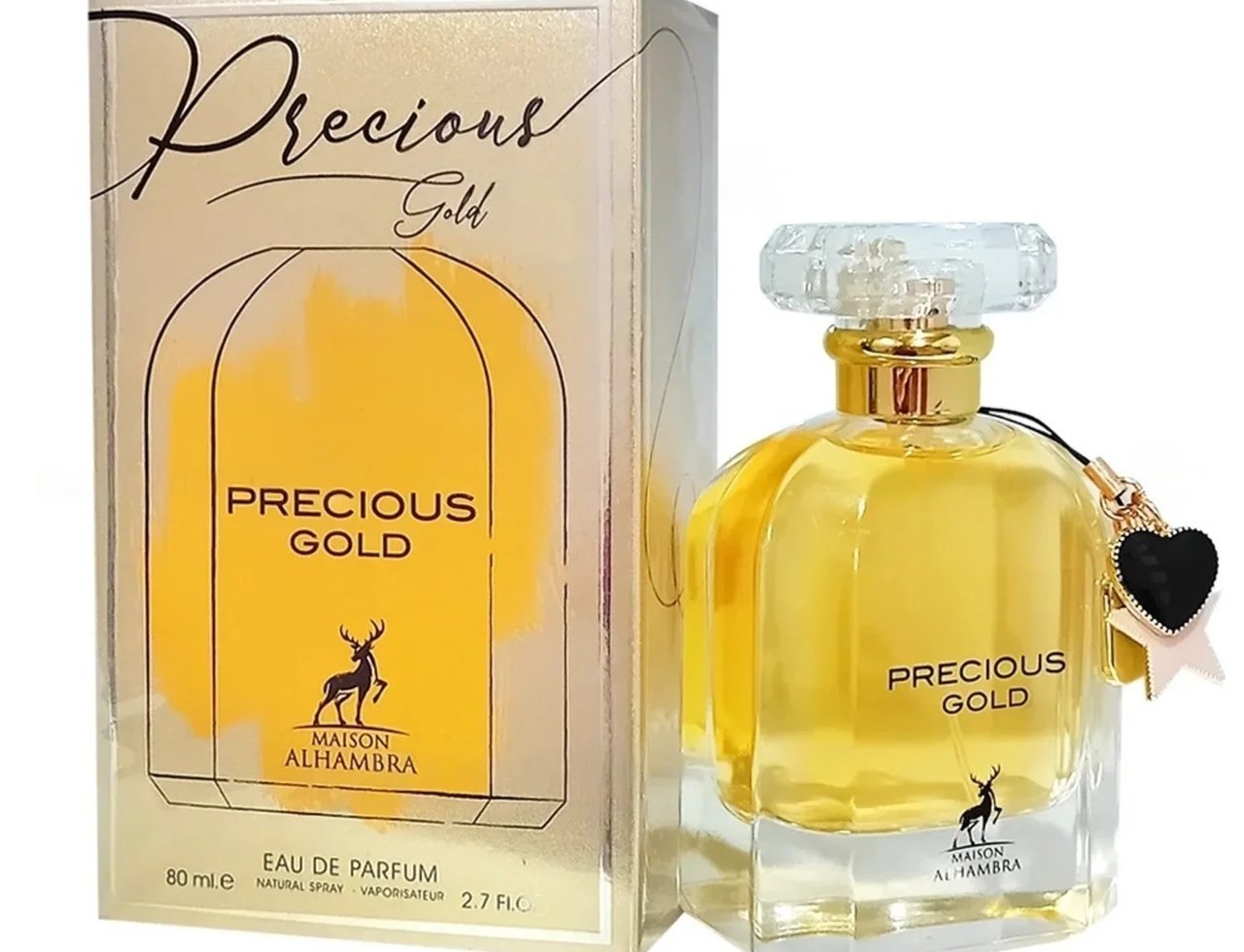 Maison Alhambra Precious Gold 80ml — A gold-toned perfume box and a clear glass bottle with gold accents and a black heart charm are displayed against a white background. | Maison Alhambra Precious Gold 80ml — Kotak minyak wangi berwarna emas dan botol kaca jernih dengan perincian emas dan loket hati hitam dipaparkan