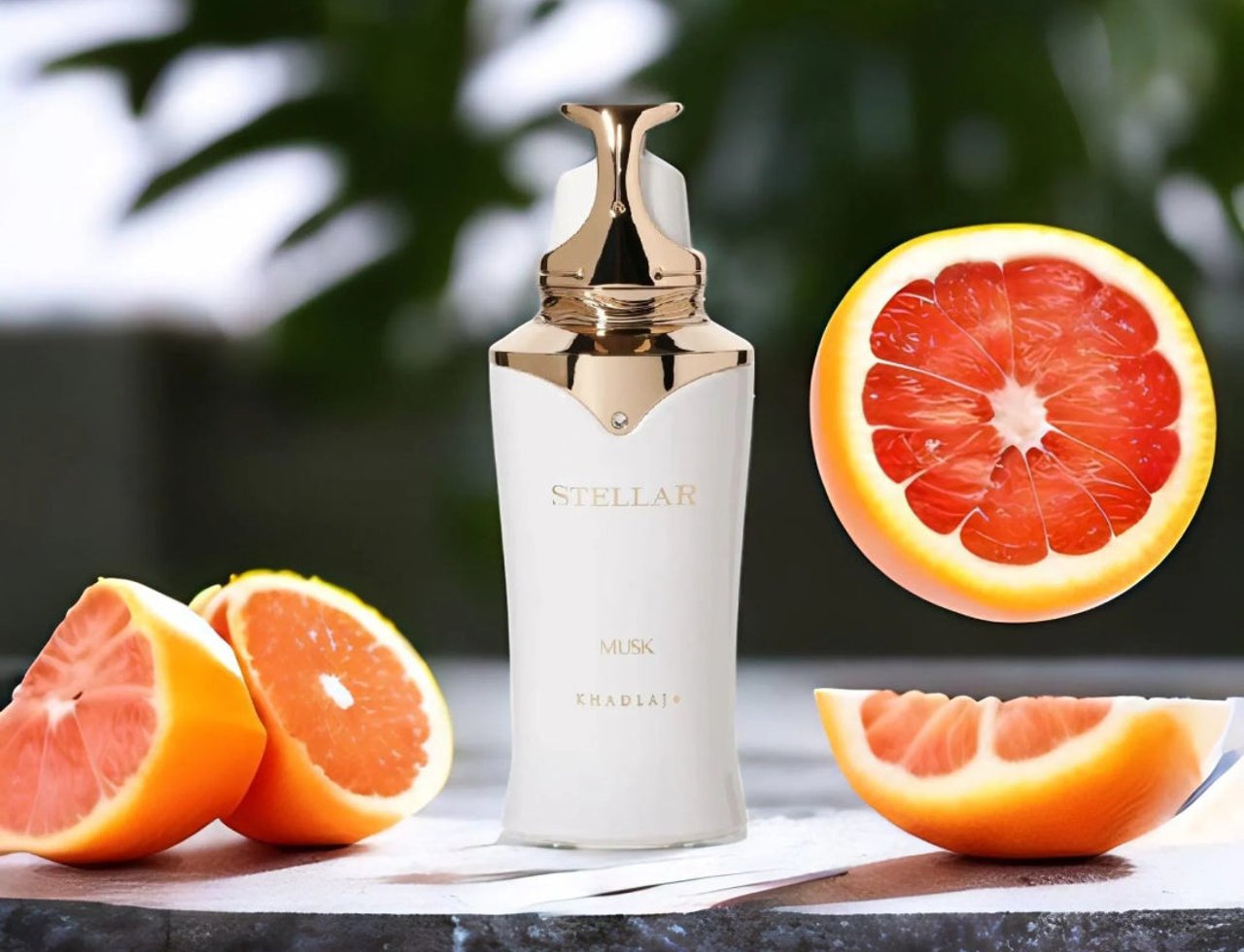 Khadlaj Stellar Musk by Khadlaj 100ml EDP — White bottle with gold accents, surrounded by grapefruit slices on a dark surface with a blurred green background.