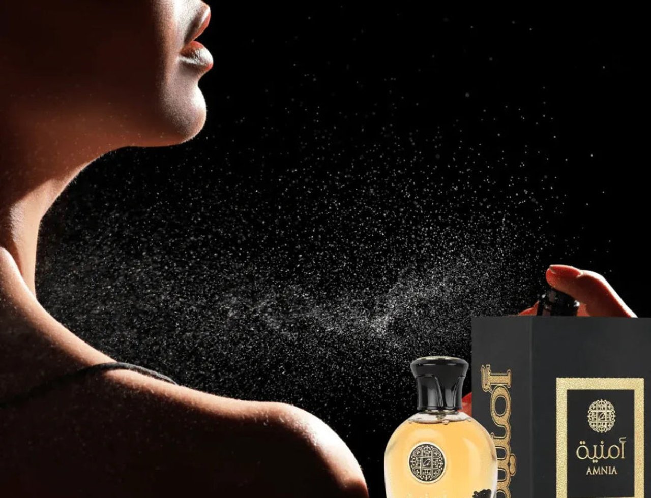 Al Wataniah Amnia by Al Wataniah For Her 100ml EDP — Wanita menyembur wangian ke lehernya, dengan botol dan kotak wangian di latar depan, latar belakang hitam.