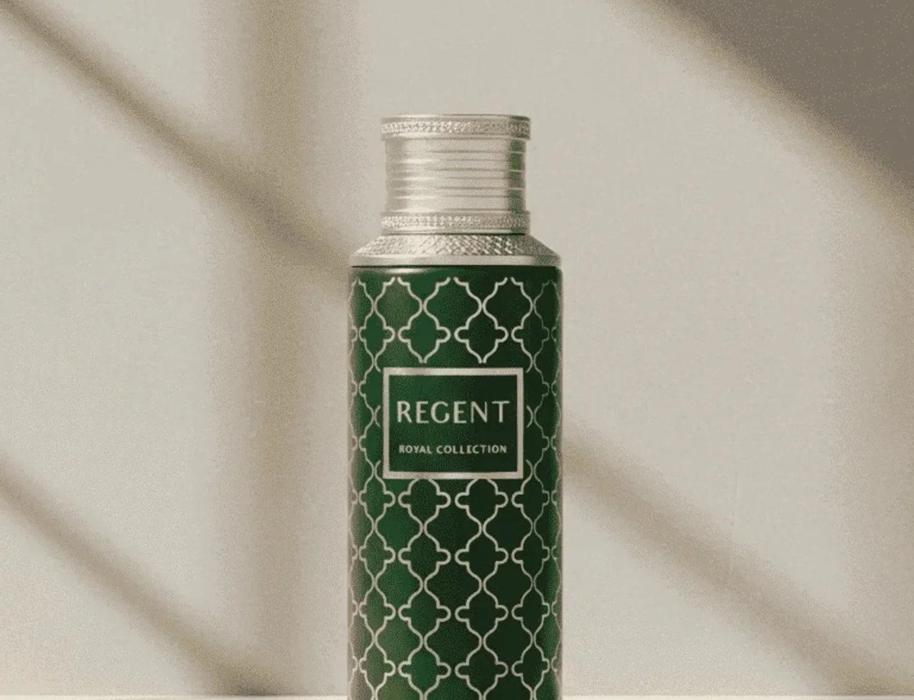 Maison Asrar Regent by Maison Asrar 100ml EDP Unisex — A tall, green bottle with a white geometric pattern and a silver ribbed cap, set against a light grey wall with dramatic shadows.