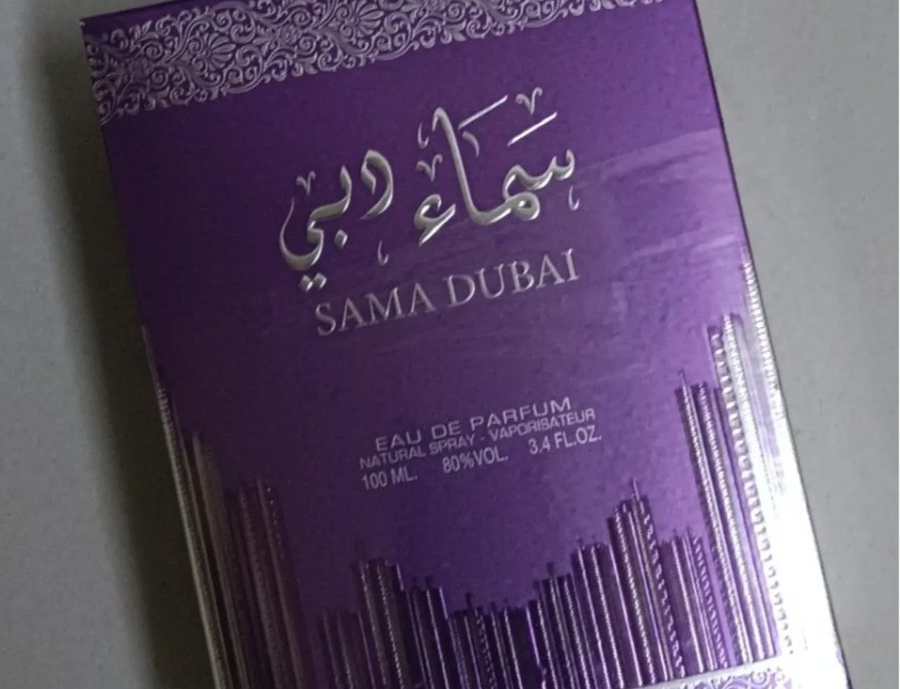 Ard Al Zaafaran Sama Dubai 100ml — Kotak wangian ungu berkilauan dengan tulisan Arab dan Inggeris 'SAMA DUBAI' serta reka bentuk bandar di bahagian bawah.