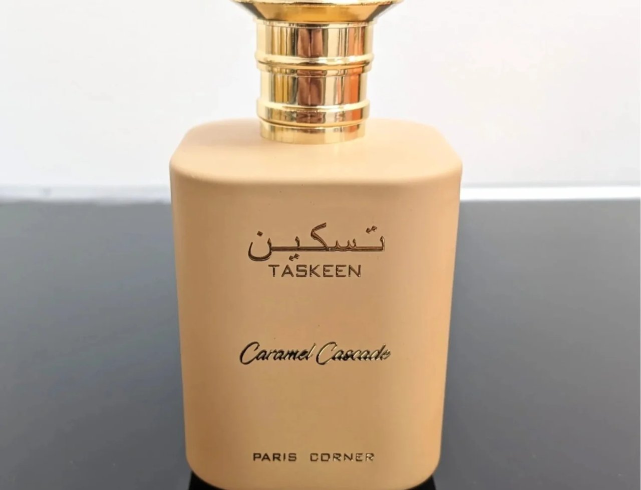 Paris Corner Taskeen Caramel Cascade — Botol wangian berwarna coklat muda dengan penutup emas berkilat, tertulis 'TASKEEN' dan 'Caramel Cascade' serta 'PARIS CORNER'
