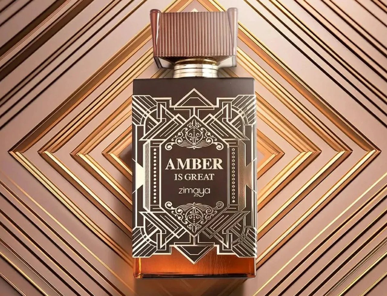 Zimaya Amber Is Great Eau De Parfum 100ml — Botol minyak wangi coklat gelap dengan penutup berjalur emas, diletakkan di atas latar belakang berjalur emas dan coklat.