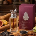 Lattafa Dynasty by Lattafa 100ml EDP Unisex — A clear glass perfume bottle with a crown-shaped silver cap, red accents, and a red stripe inside, sits next to its burgundy box. Citrus slices, dried tea leaves, and spices are arranged around it.