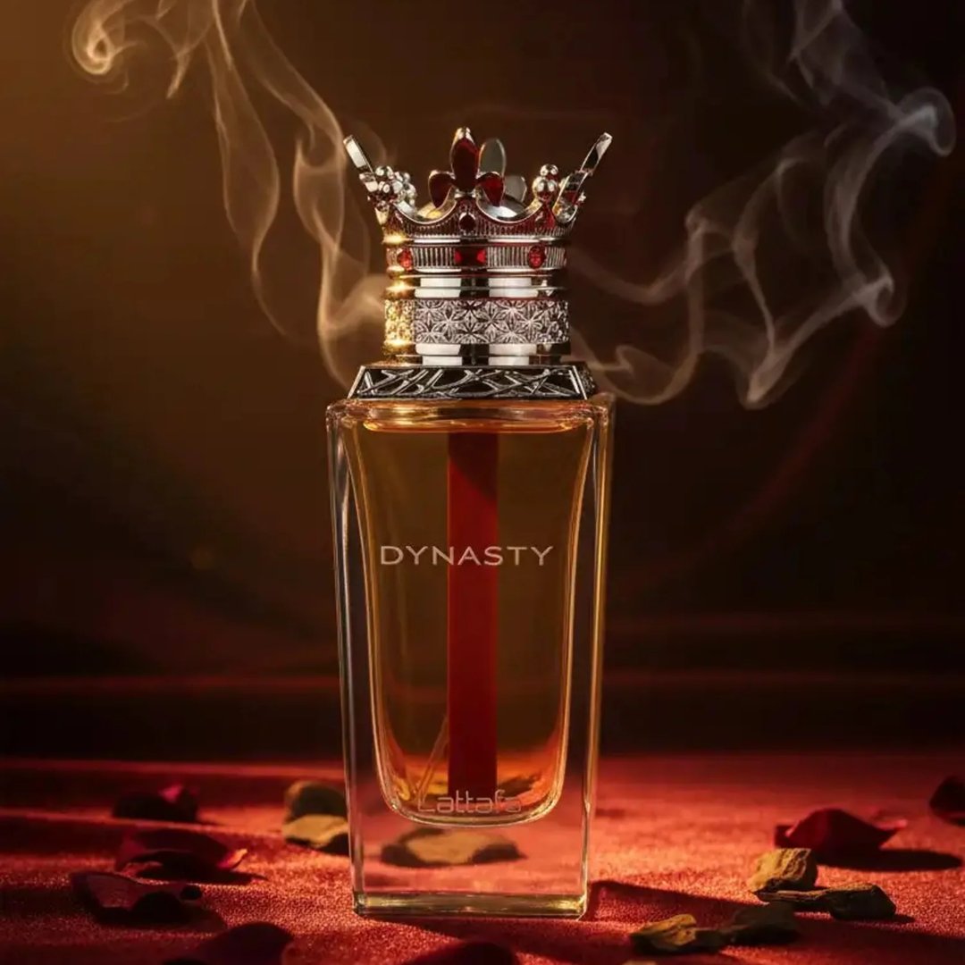 Lattafa Dynasty by Lattafa 100ml EDP Unisex — A luxurious perfume bottle with a crown-shaped cap, set against a dark, smoky background with red velvet and scattered rose petals.