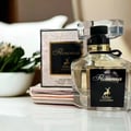 Maison Alhambra Florenza (Florence) 100ml by Maison Alhambra — A clear glass perfume bottle with a black label featuring a gold deer logo and the name 'Florenza' in script, placed next to its matching box on a white surface. | Maison Alhambra Florenza (Florence) 100ml oleh Maison Alhambra — Botol minyak wangi kaca