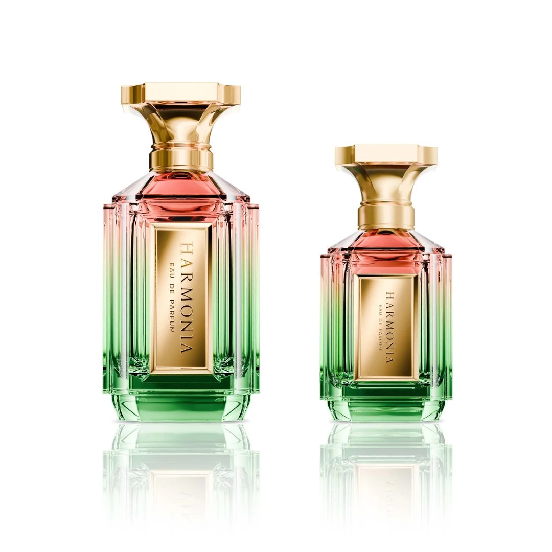 Velixir Harmonia Velixir Parfums 100ml for Unisex — Two glass perfume bottles with a gradient of pink to green liquid, gold caps, and gold labels, displayed side-by-side on a white reflective surface. | Velixir Harmonia Velixir Parfums 100ml untuk Unisex — Dua botol minyak wangi kaca dengan gradien cecair merah jambu