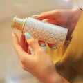 Maison Asrar Heritage by Maison Asrar 100ml EDP Unisex — Tangan memegang botol minyak wangi putih bercorak geometri emas dan penutup emas.