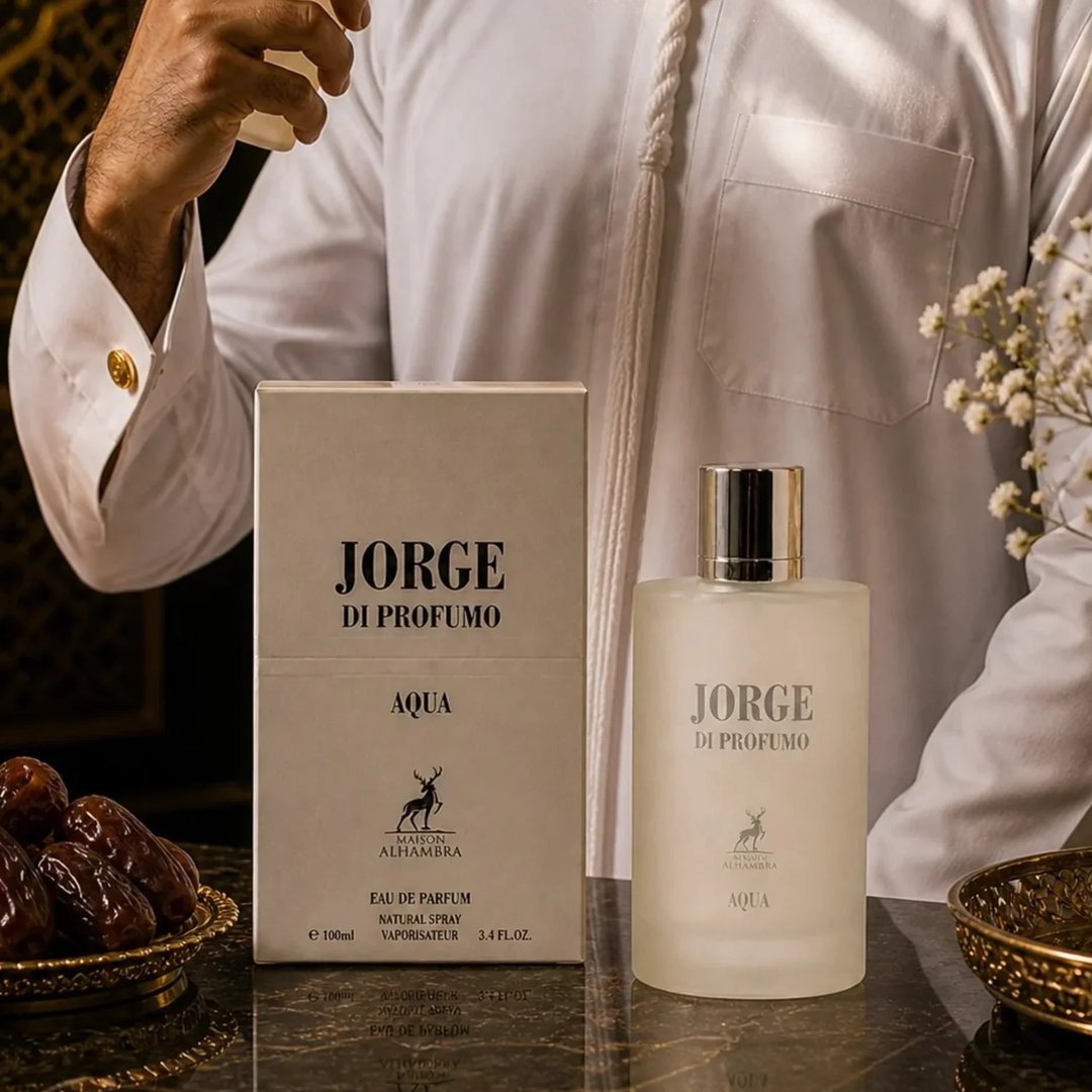 Maison Alhambra Jorge Di Profumo Aqua — A man in a white thobe with gold cufflinks is holding a perfume bottle and box, with dates and flowers nearby. | Maison Alhambra Jorge Di Profumo Aqua — Seorang lelaki memakai jubbah putih berserta cufflink emas sedang memegang botol dan kotak minyak wangi, dengan kurma dan