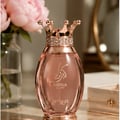 Zimaya Kibria Glory — Botol minyak wangi rose gold dengan penutup bentuk mahkota bertatah kristal, latar belakang lembut dengan bunga peony merah jambu dan cermin emas.